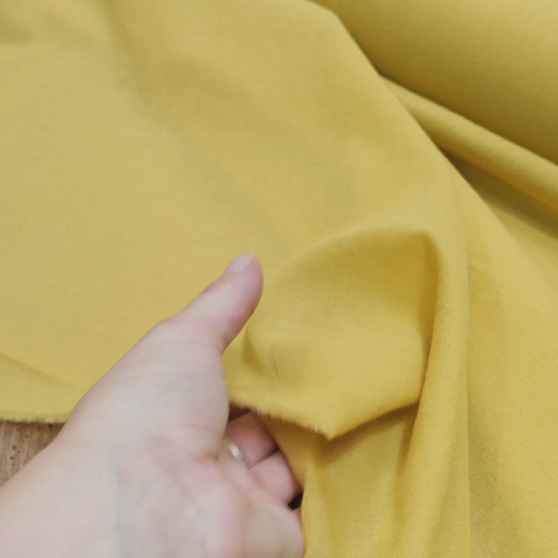 Hand crumples yellow cotton fabric with a soft, slightly creased texture.