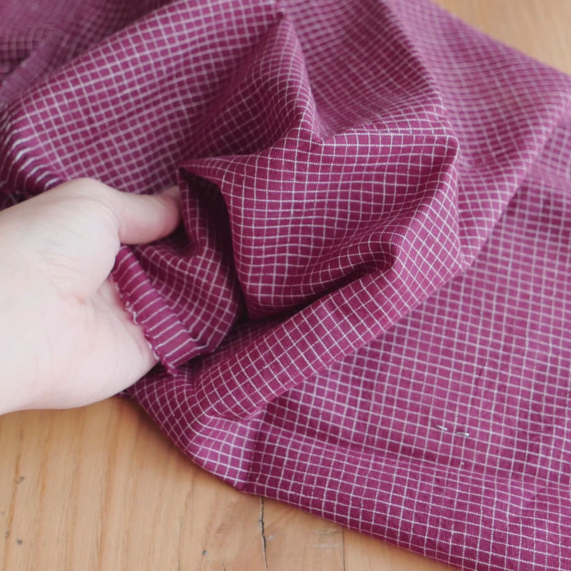 Plum coloured fabric woven with a white grid. 