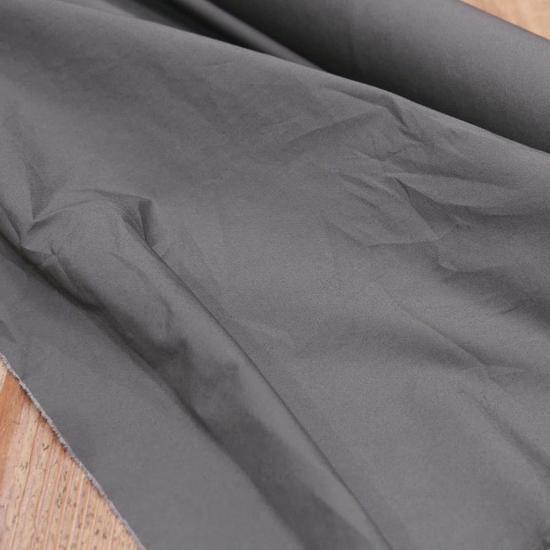 A hand crumples crisp grey cotton fabric.