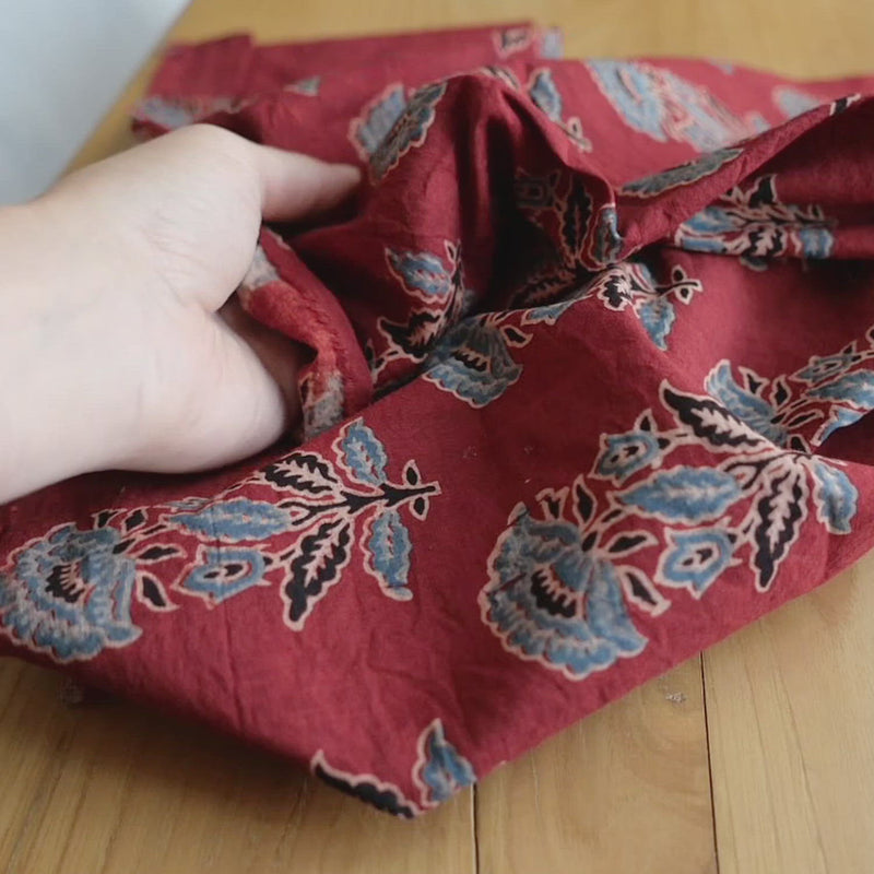 Hand crumples red cotton with blue poppies.