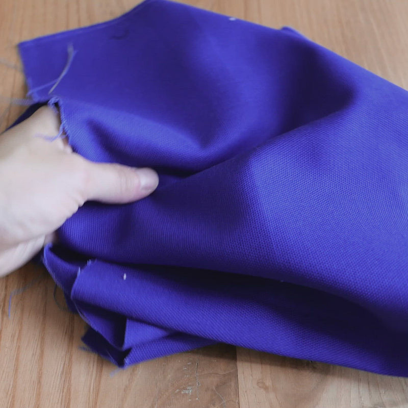 Hand crumples stiff blue canvas fabric.