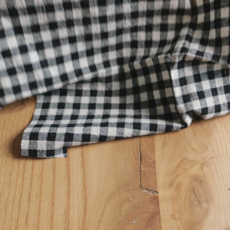 Hand crumples black and white gingham fabric. The fabric has a soft, linen-like texture.