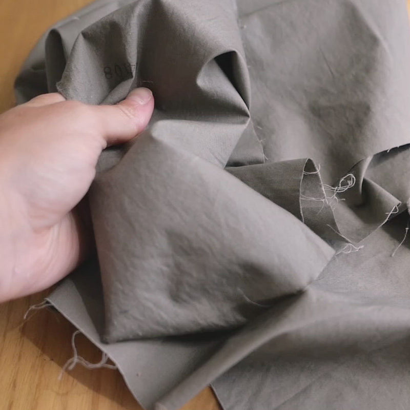 Hand crumples creased grey cotton with a fine, crisp texture.