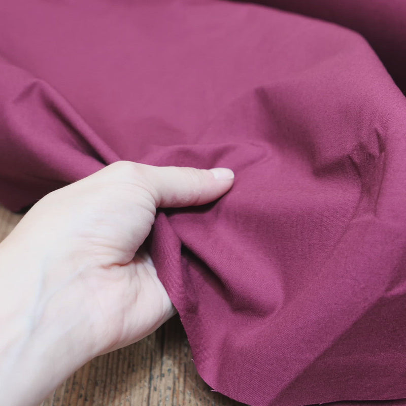 Hand crumples maroon cotton drill, with a smooth, fine texture.