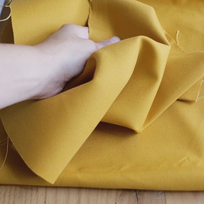 Hand crumples stiff canvas fabric in a mustard colour.