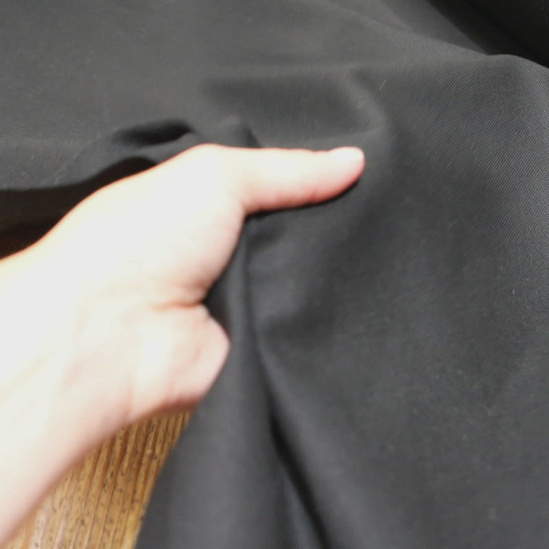 Hand crumples stiff black canvas fabric.