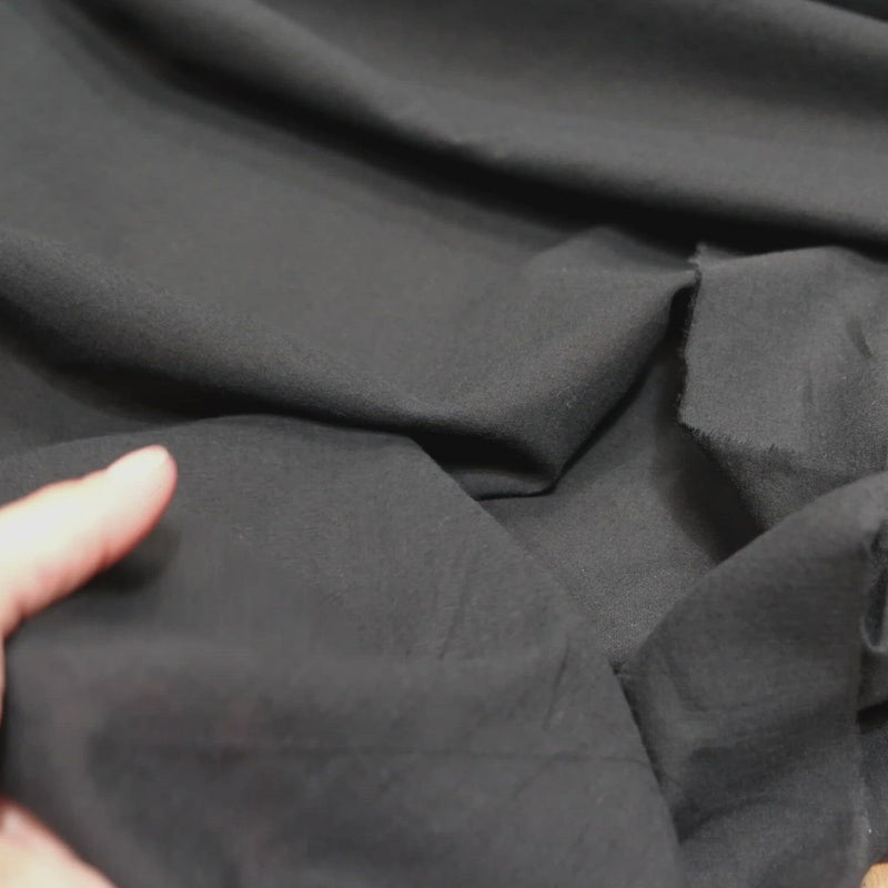 Hand crumples fine black cotton fabric.