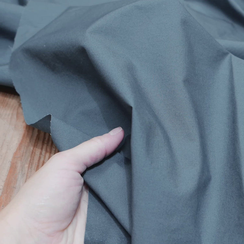 Hand crumples teal grey cotton fabric. The fabric has a fine, crisp texture.