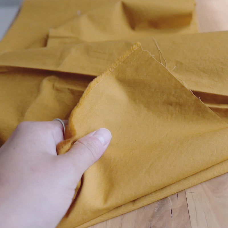 Hand crumples mustard cotton fabric with a fine, crisp texture.