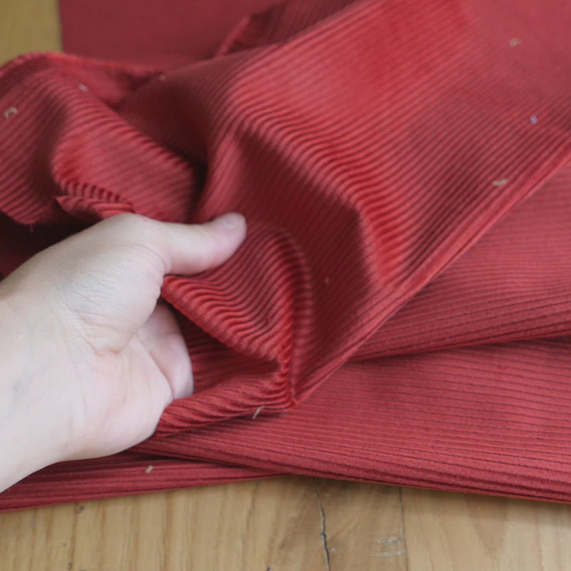 Hand crumples red corduroy. The fabric has a slight sheen.