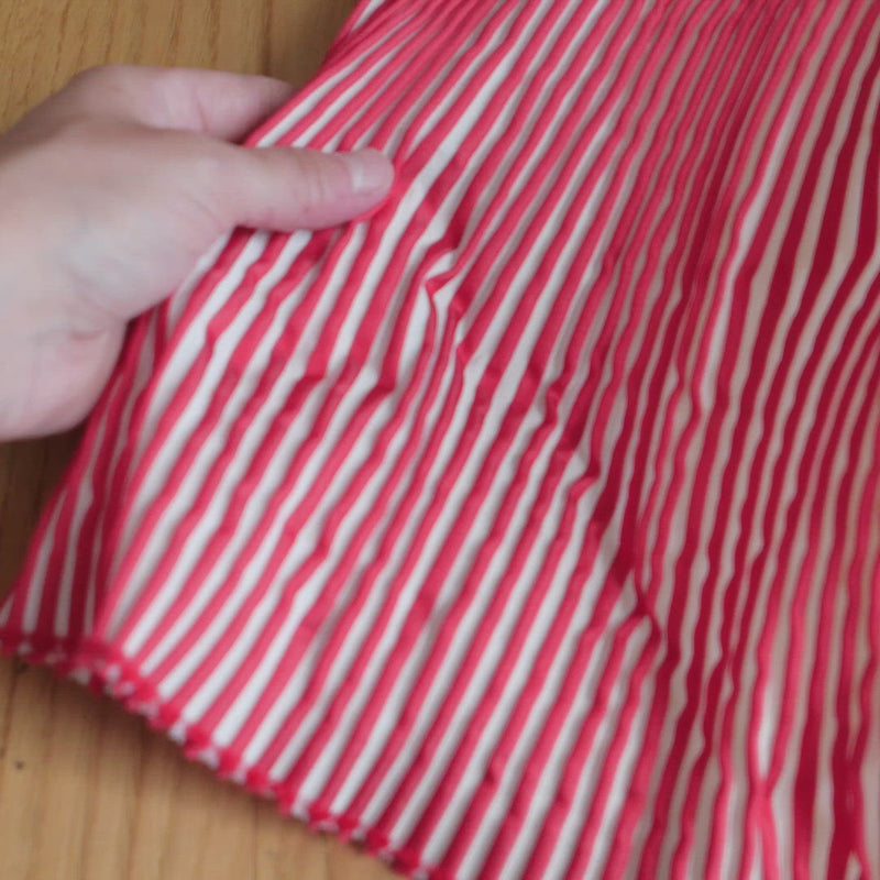 Hand crumples red and white striped fabric. The fabric has a corrugated texture and folds along the strips like an accordion.