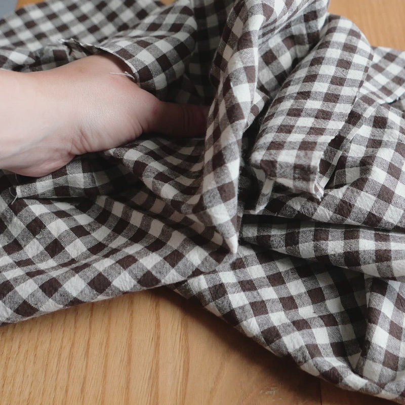 Hand crumples brown and white gingham fabric. The fabric has a soft, linen-like texture.