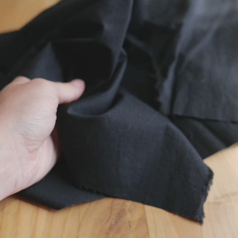 A hand crumples black cotton fabric, with a soft, crisp texture.