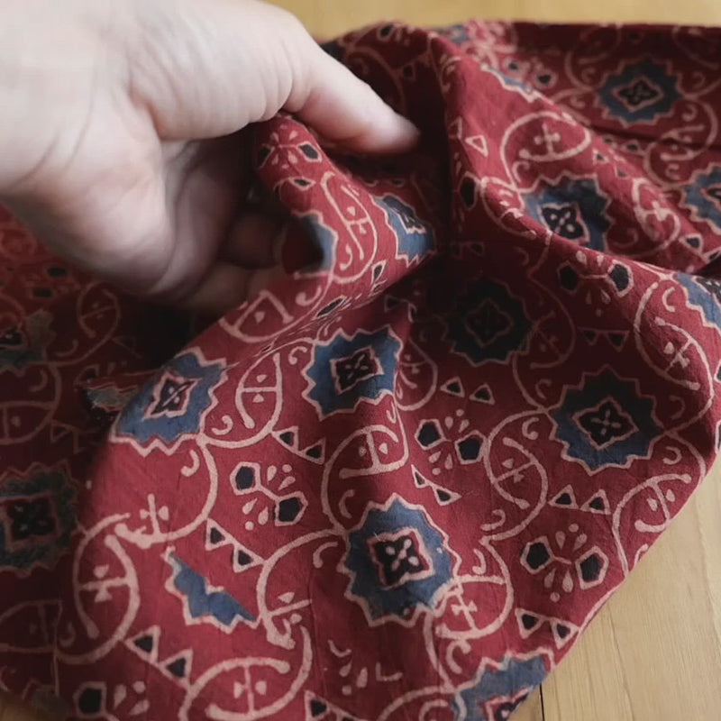 Hand crumples red patterned cotton.