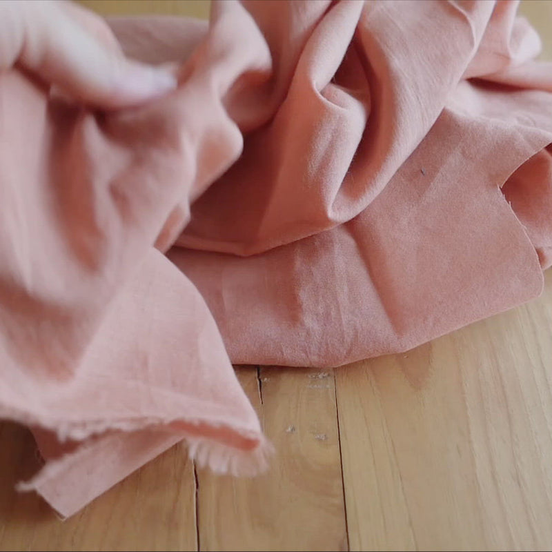 Hand crumples peach coloured cotton fabric.