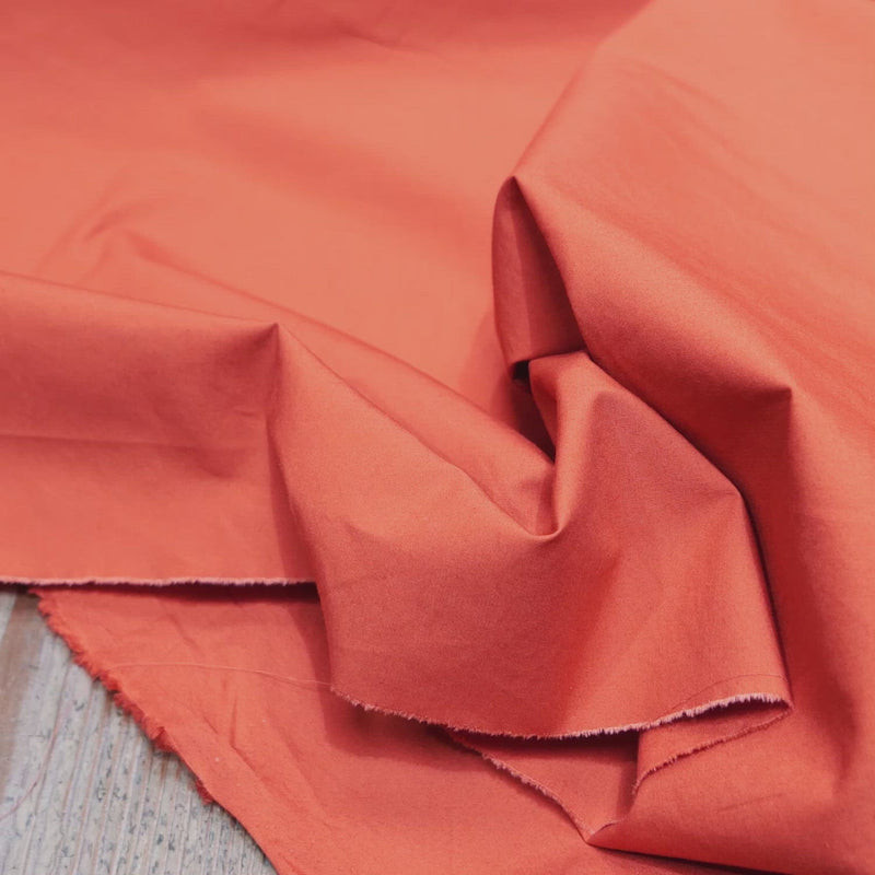 Hand crumples orange cotton fabric with a fine, crisp texture.