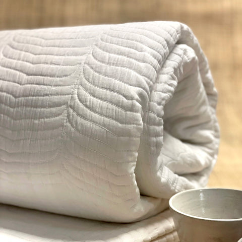 A plain white cotton blanket, quilted in a scallop pattern. 