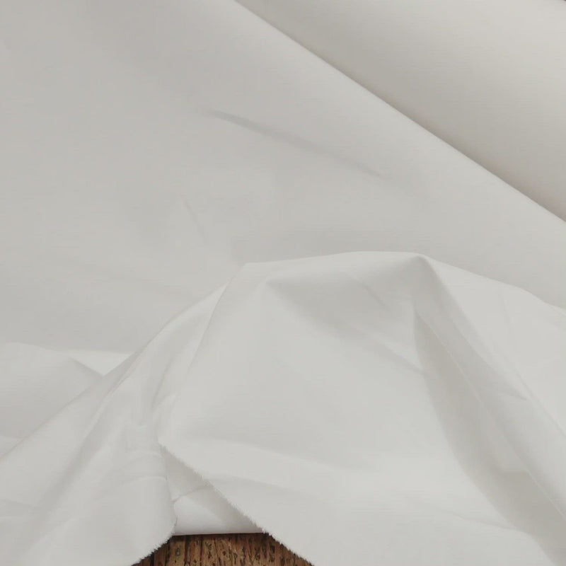 Hand crumples white cotton fabric. The fabric has a fine, crisp texture.