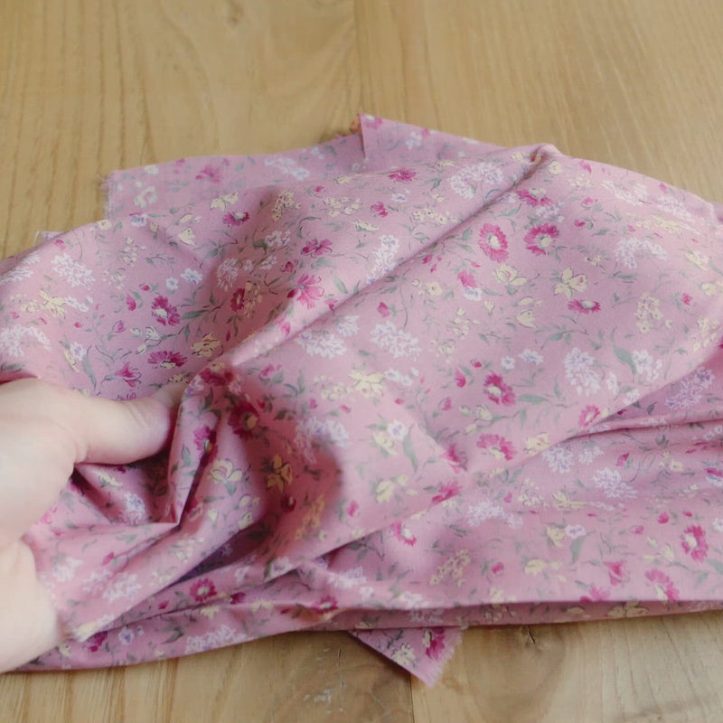 Pink fabric printed with a small vintage floral pattern.