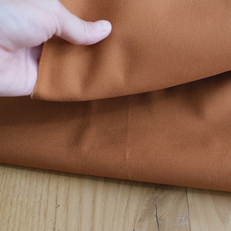 Hand crumples stiff orange canvas.