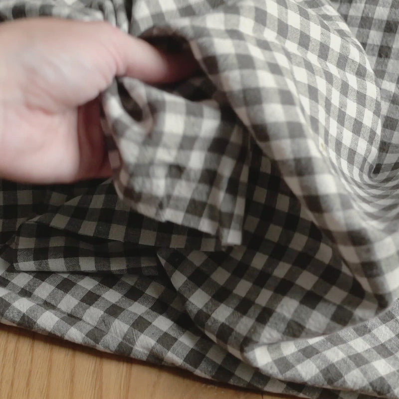 Hand crumples white and khaki gingham fabric. The fabric has a soft, linen-like texture.