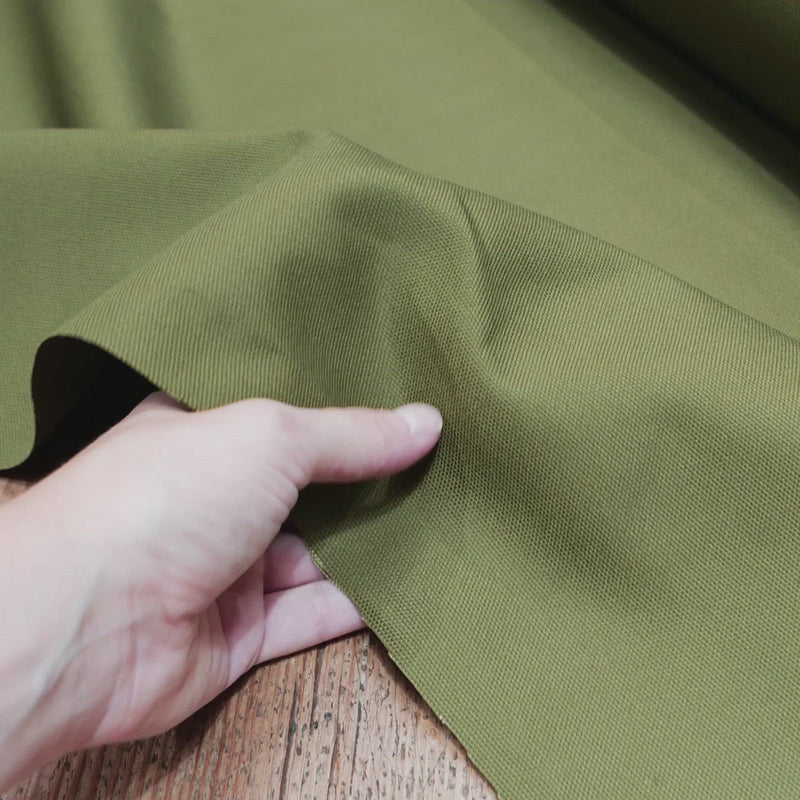 Hand crumples stiff, green canvas fabric.