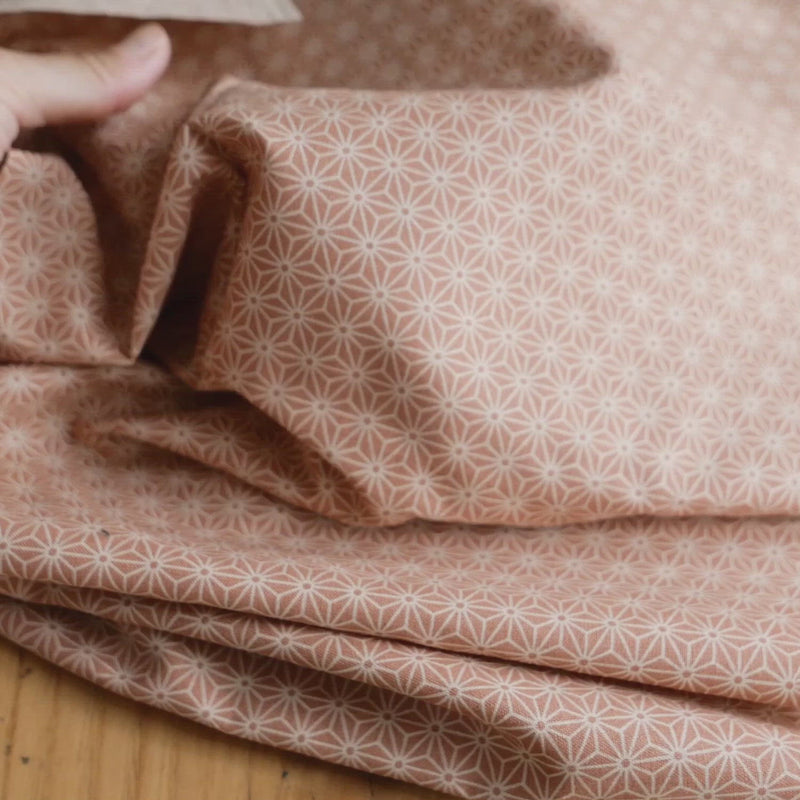 Hand crumples pink and white patterned fabric.